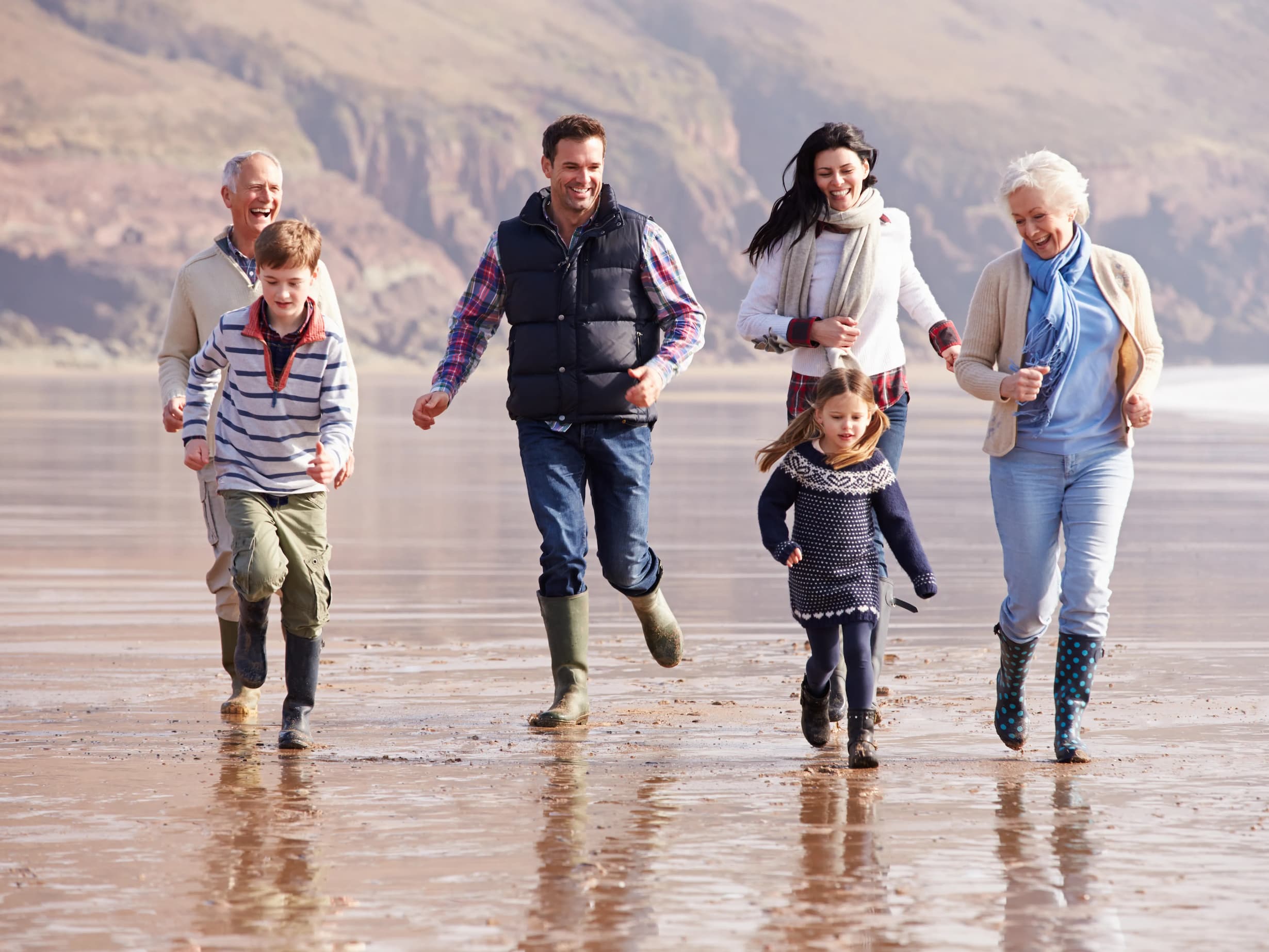 Multi generation family running on winter beach using hearing aids